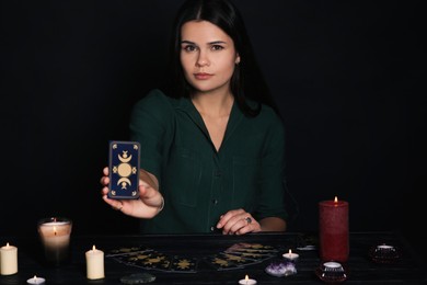 Photo of Soothsayer showing tarot card at table on black background. Fortune telling