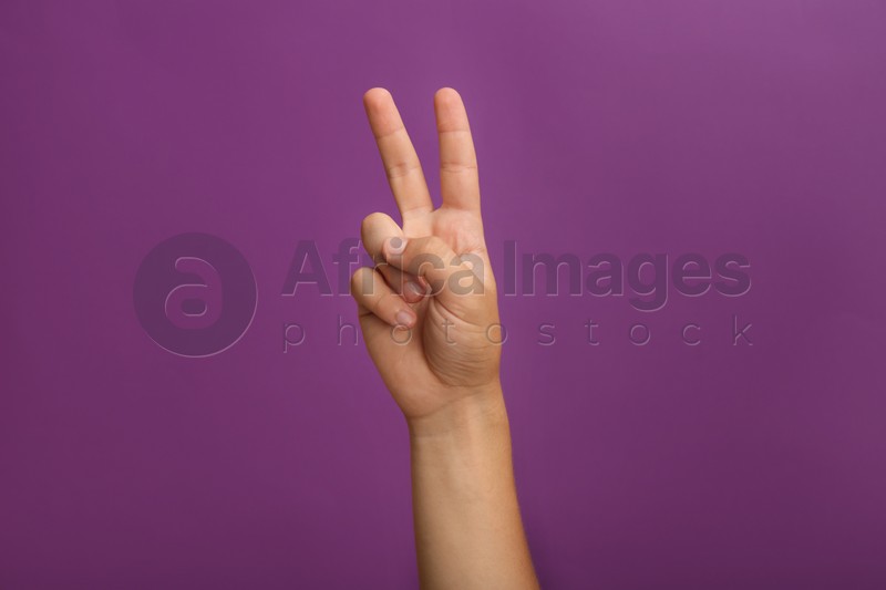 Photo of Teenage boy showing two fingers on purple background, closeup