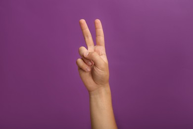 Teenage boy showing two fingers on purple background, closeup