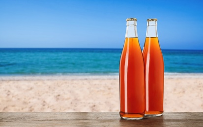 Bottles of delicious kvass on wooden table near sea. Space for text