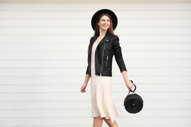 Beautiful young woman with stylish handbag near white wall