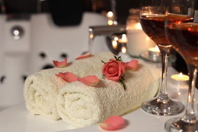 Glasses of wine, towels and rose on tub in bathroom, closeup. Romantic atmosphere