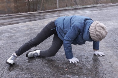 Young woman having difficulties with moving on icy road outdoors