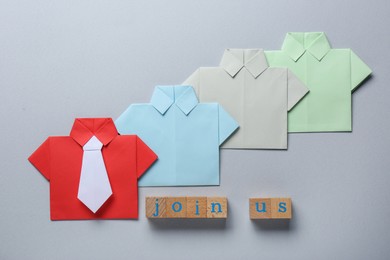 Photo of Many paper shirts and phrase Join Us made with wooden cubes on white background, flat lay. Recruiter searching employee
