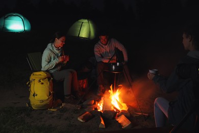 Friends sitting around bonfire outdoors in evening. Camping season