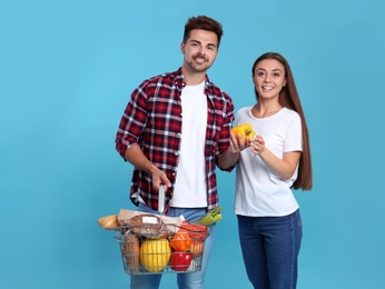 Young couple with shopping basket full of products on blue background