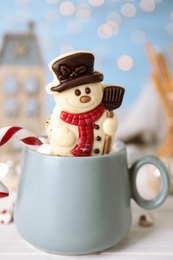 Funny chocolate snowman candy in cup of hot drink on white table
