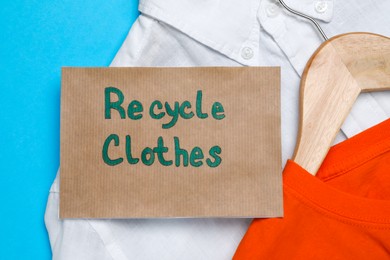 Different clothes with recycling label on light blue background, flat lay