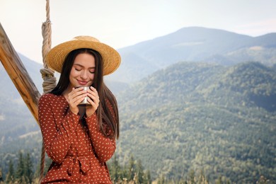 Young woman with hot drink resting in mountains on sunny day