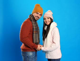 Happy young couple in warm clothes on blue background. Winter vacation