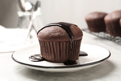 Delicious fresh cupcake with chocolate syrup on light grey marble table, closeup