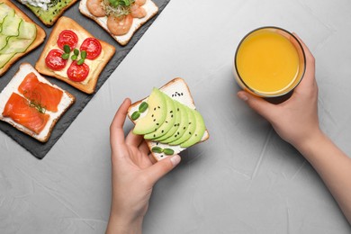 Photo of Woman holding delicious toast and glass of juice at light grey table, top view
