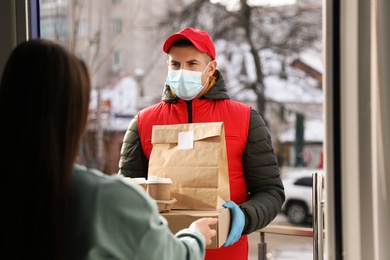 Courier in medical mask giving to woman her order at doorway. Delivery service during Covid-19 quarantine