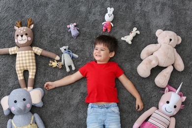Photo of Cute little boy and soft toys on floor, top view