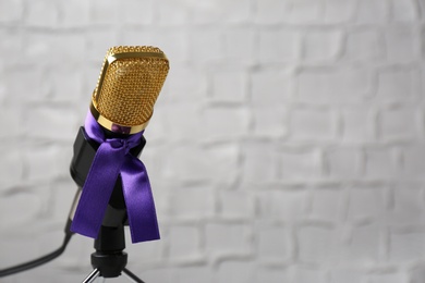 Microphone with purple awareness ribbon against white wall, space for text