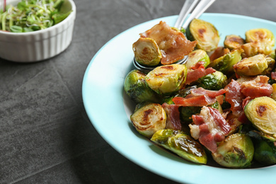 Delicious roasted Brussels sprouts with bacon served on black table, closeup