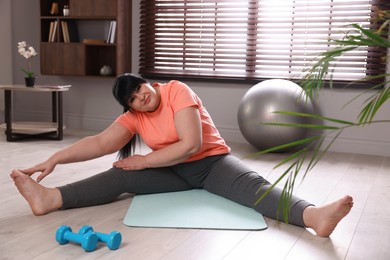 Overweight mature woman stretching on yoga mat at home