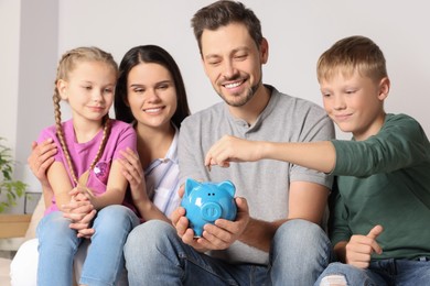 Photo of Happy family putting coin into piggy bank at home