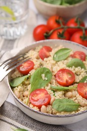 Photo of Delicious quinoa salad with tomatoes, beans and spinach leaves served on table, closeup