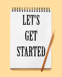 Image of Notebook with phrase LET'S GET STARTED on yellow background, top view