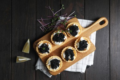 Photo of Board of delicious tartlets with black caviar and cream cheese on wooden table, top view