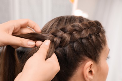 Professional stylist braiding client's hair in salon, closeup