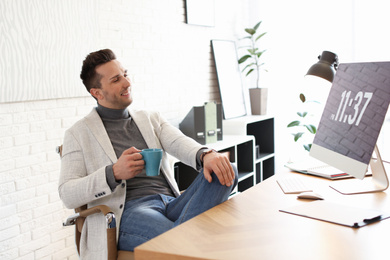 Young man with cup of drink relaxing at table in office during break