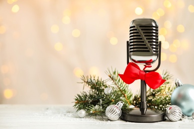 Microphone with red bow and decorations on white table against blurred lights, space for text. Christmas music