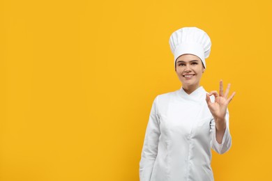 Photo of Happy female chef showing ok gesture on orange background. Space for text