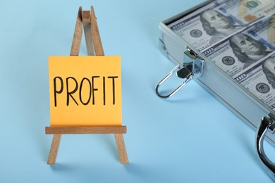 Economic profit. Easel with note and banknotes in briefcase on light blue background, closeup
