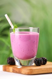 Delicious blackberry smoothie in glass and berries on white table