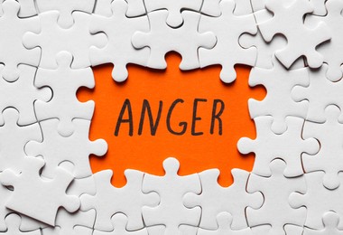 White puzzle pieces and word ANGER written on orange background, flat lay