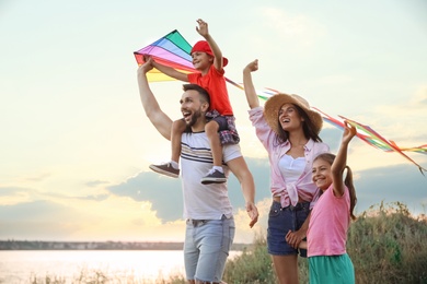Happy parents and their children playing with kites outdoors at sunset. Spending time in nature