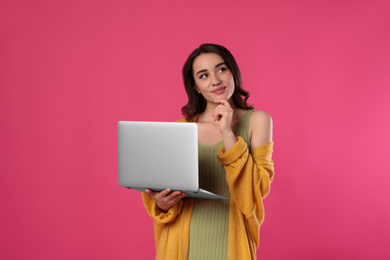 Pensive young woman with laptop on pink background