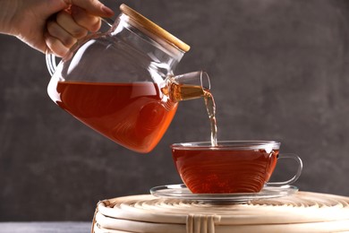 Photo of Woman pouring freshly brewed tea into glass cup on wicker table, closeup