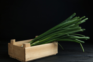 Fresh green spring onions in crate on black wooden table