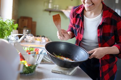 Young woman holding pan with freshly fried eggs and vegetables in kitchen, closeup