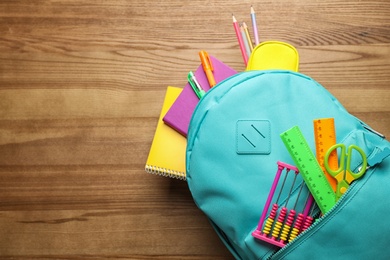 Stylish backpack with different school stationary on wooden table, top view. Space for text