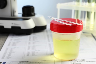Container with urine sample for analysis on test forms in laboratory, closeup