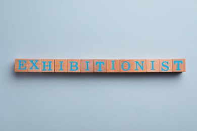 Word EXHIBITIONIST made with wooden cubes on white background, flat lay