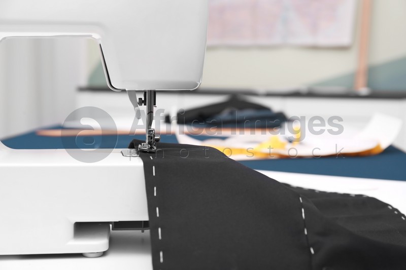 Photo of Sewing machine with fabric on table in tailor workshop, closeup