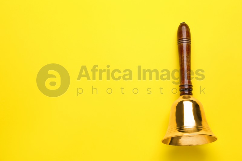 Golden school bell with wooden handle on yellow background, top view. Space for text
