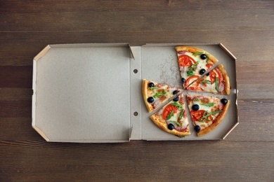 Cardboard box with tasty pizza on wooden background, top view