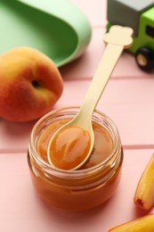 Spoon with healthy baby food and glass jar on pink wooden table, closeup