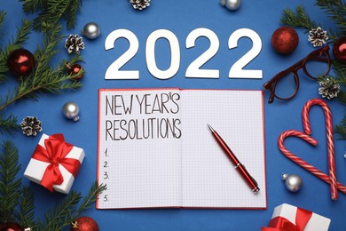 Making New Year's resolutions. Flat lay composition with notebook, 2022 numbers and festive decor on blue background