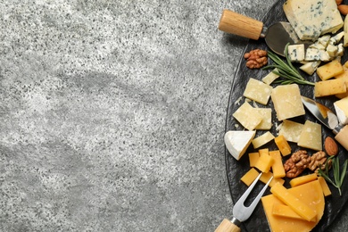 Cheese platter with specialized knives and fork on grey table, top view. Space for text