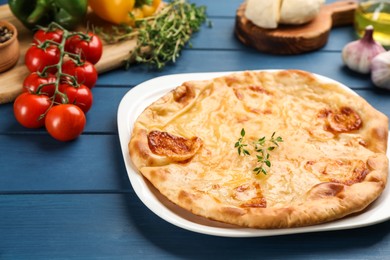 Delicious khachapuri with cheese, thyme and vegetables on blue wooden table, closeup