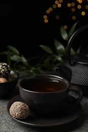 Cup of aromatic tea and delicious vegan candy ball on grey table against blurred lights, space for text