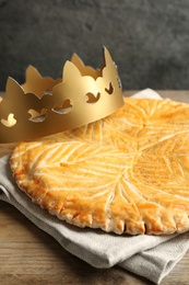 Traditional galette des Rois with paper crown on wooden table, closeup