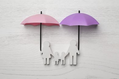 Small umbrellas and family figure on white wooden background, flat lay